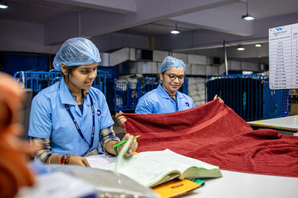 Two female textile workers inspecting red fabric in a factory setting.