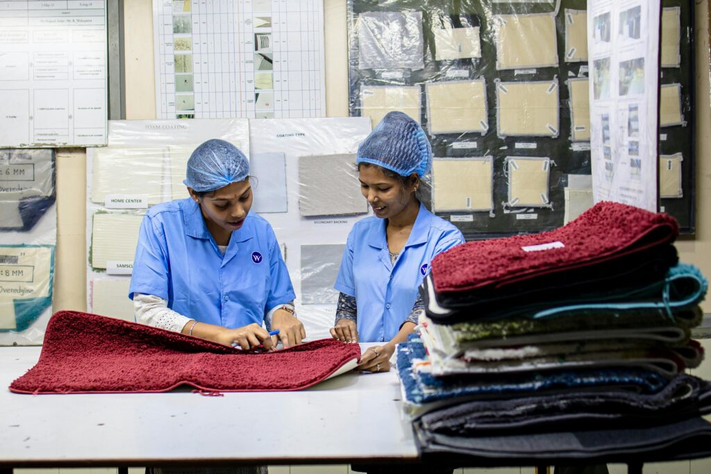 Two women in a textile factory inspecting red fabric samples in an industrial setting.